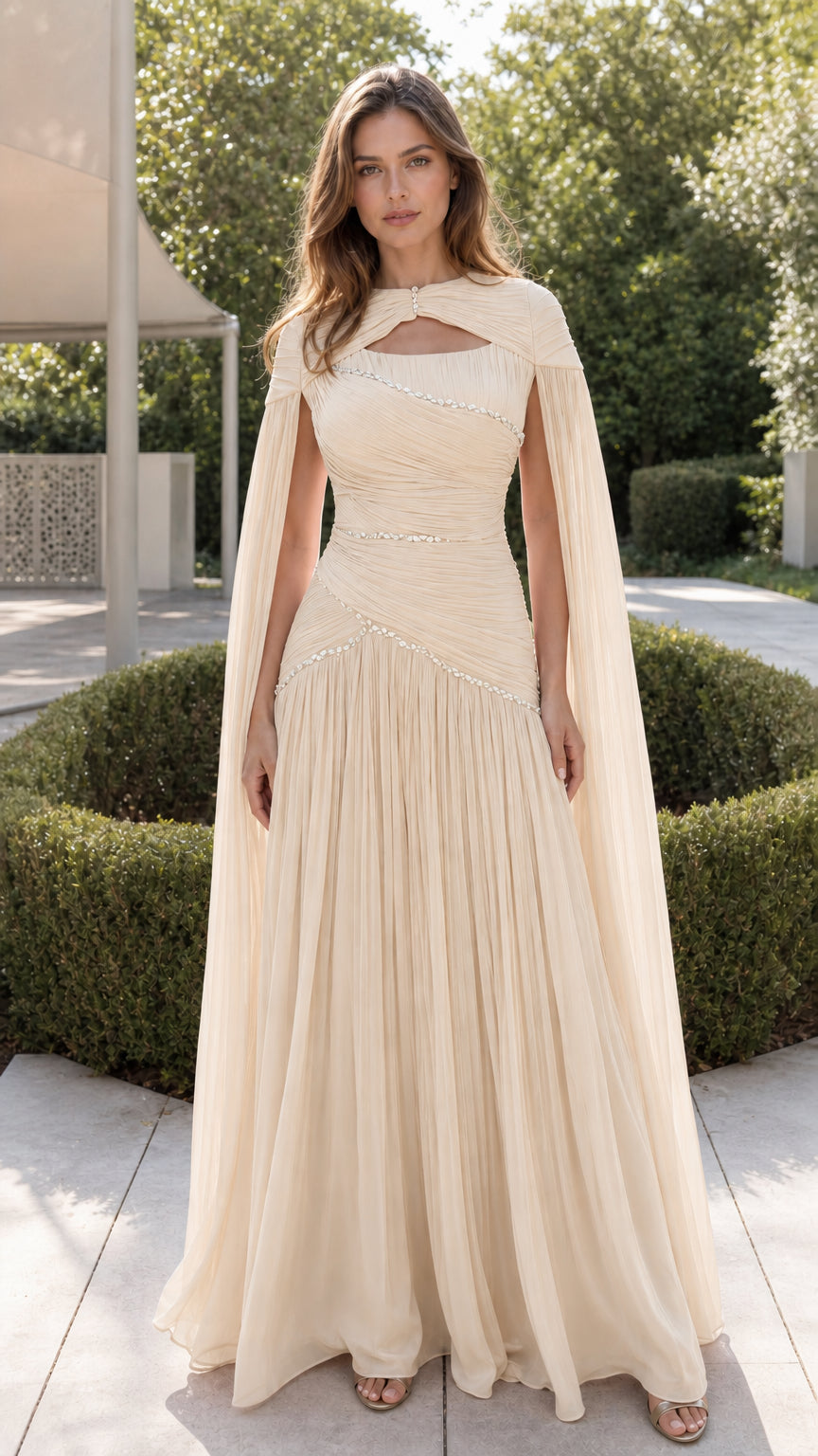 Front view of champagne cream pleated chiffon cape gown with rhinestone details