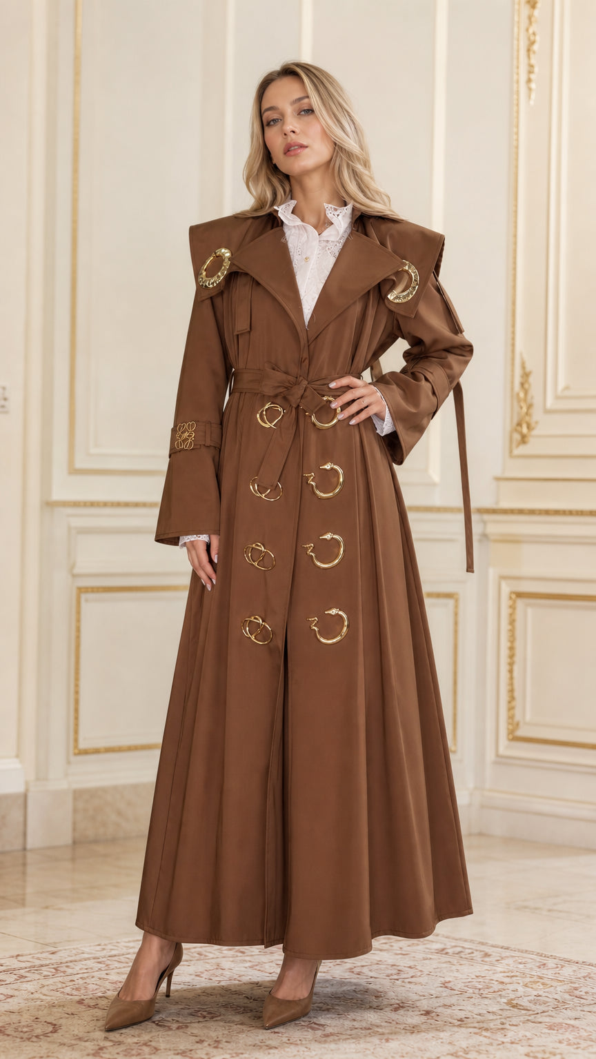 Full-length front view of woman wearing brown maxi belted trench coat with gold hardware