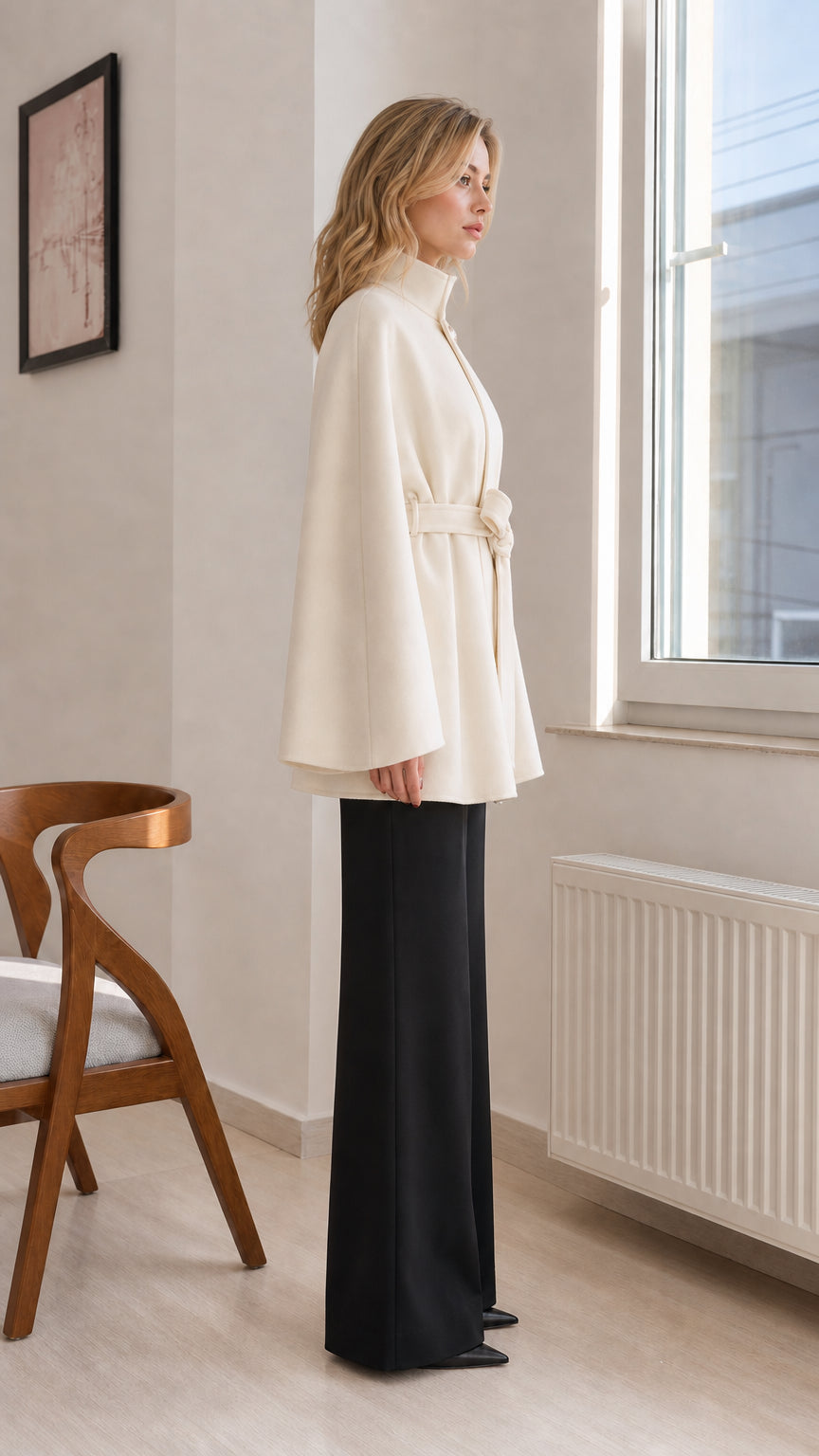 Side profile view of cream stand-collar cape coat showing draped sleeve design