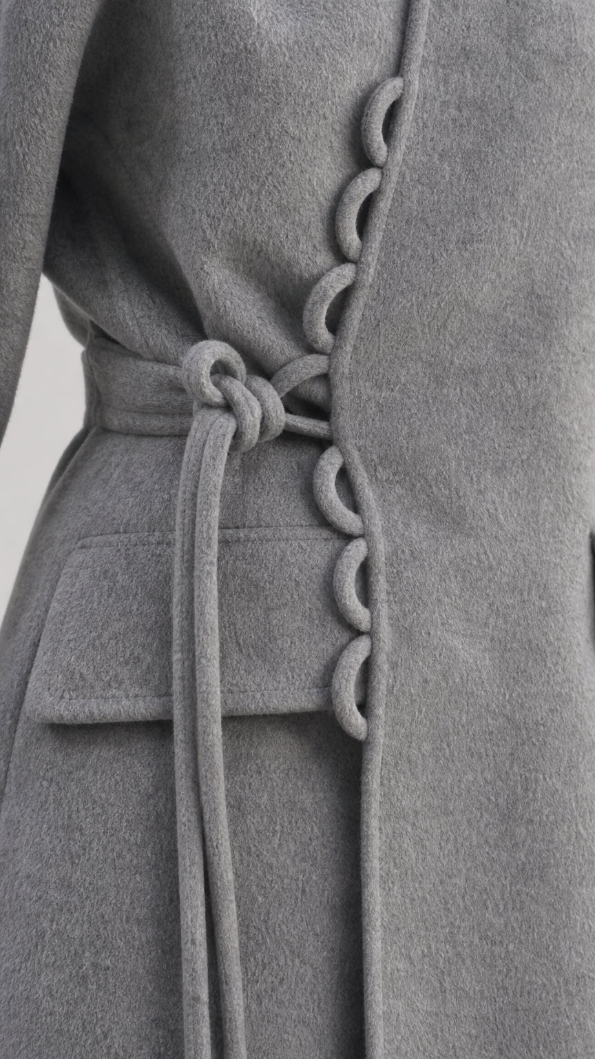 Close-up of the gray wrap coat's decorative loop buttons, waist tie, and flap pocket