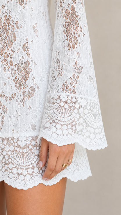 Close-up detail of white floral lace fabric, flared bell sleeve, and scalloped hem