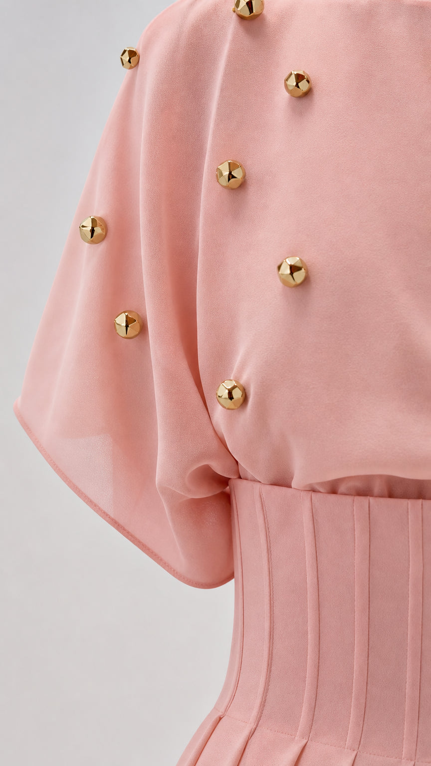 Close-up detail of blush pink sleeve fabric, gold-tone studs, and pleated waistband