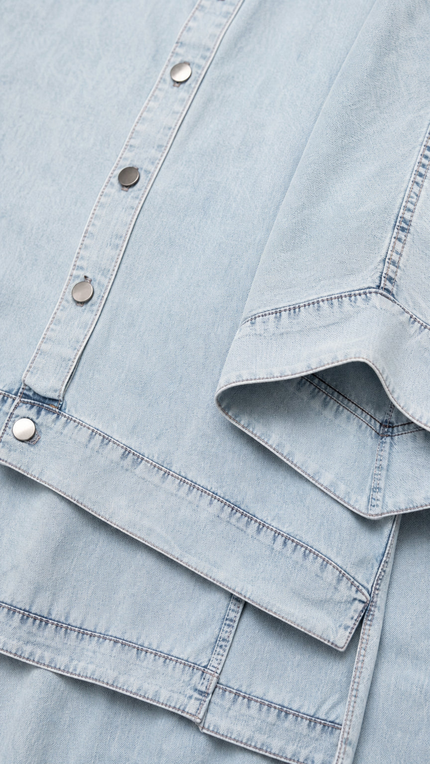 Close-up detail of light blue fabric, buttons, and seaming on shirt