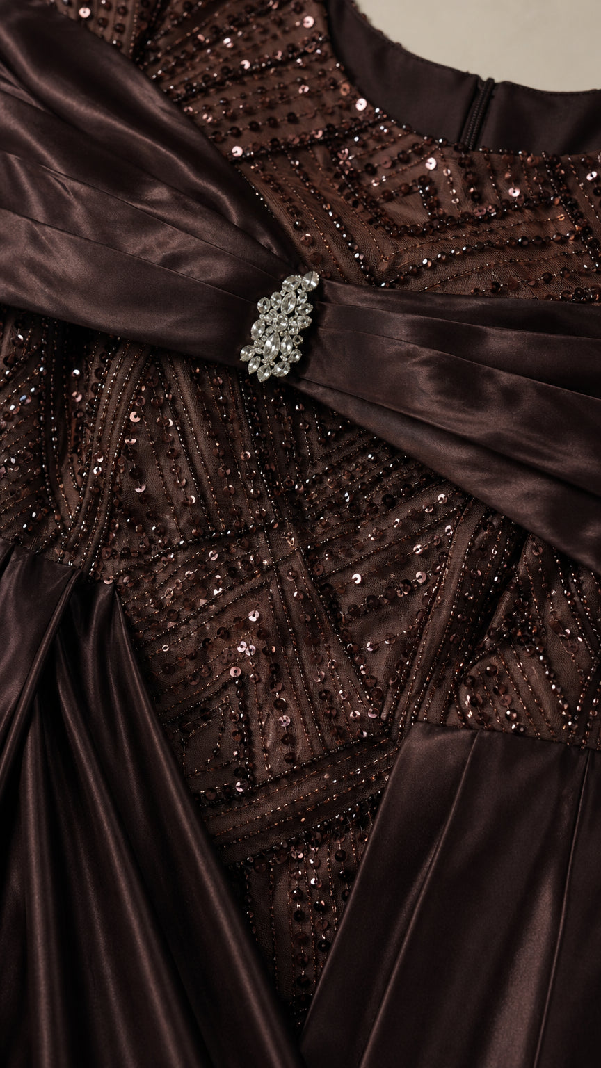 Close-up detail of geometric sequin patterns, satin chest drape, and sparkling crystal brooch