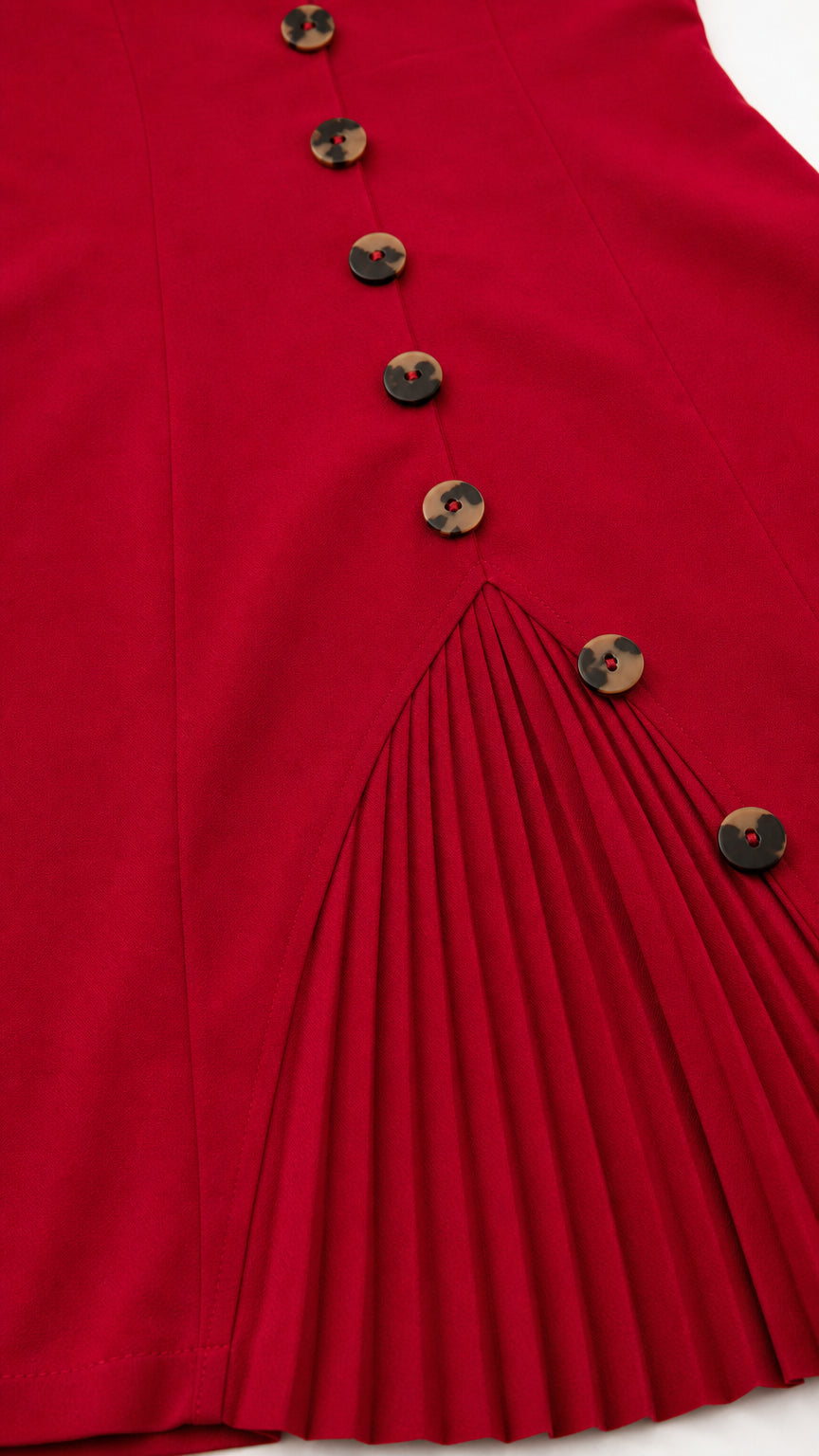 Close-up detail of tortoiseshell buttons and sharp knife pleats on the red dress hem