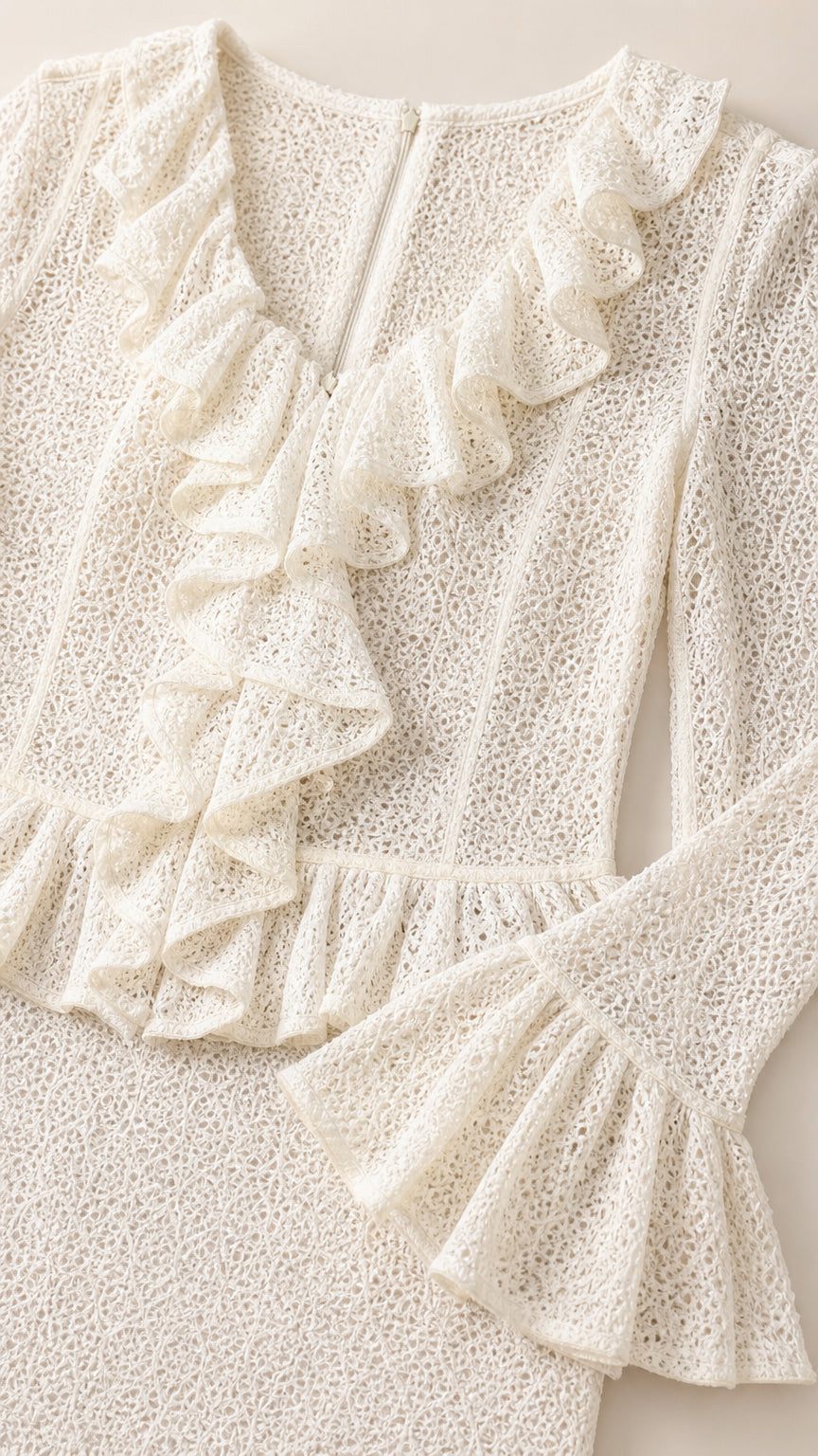 Close-up detail of textured cream lace fabric with ruffle neckline and sleeve cuff