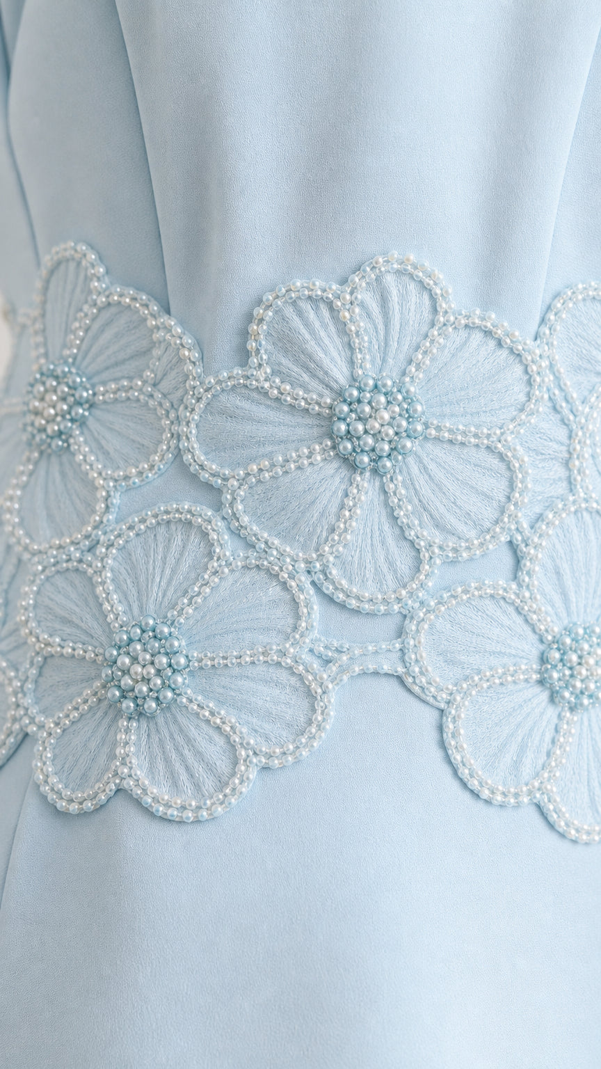 Close-up detail of light blue floral embroidery and pearl bead embellishment
