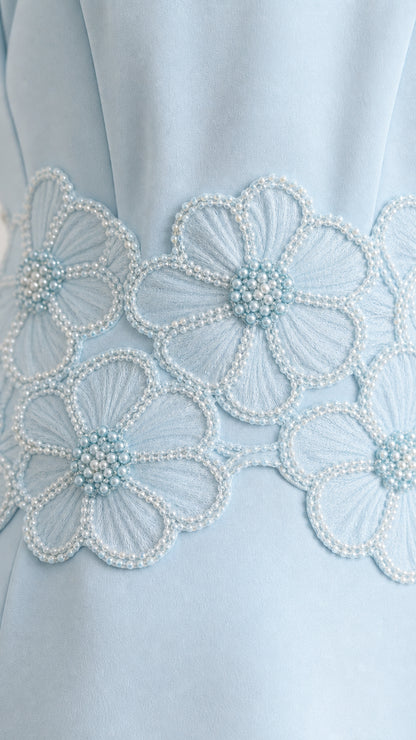 Close-up detail of light blue floral embroidery and pearl bead embellishment