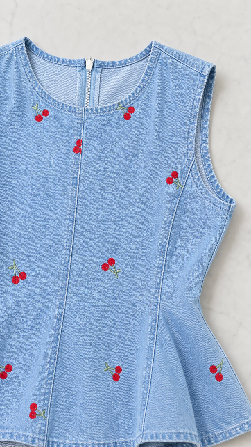 Close-up detail of light blue denim peplum top with cherry embroidery and back zipper