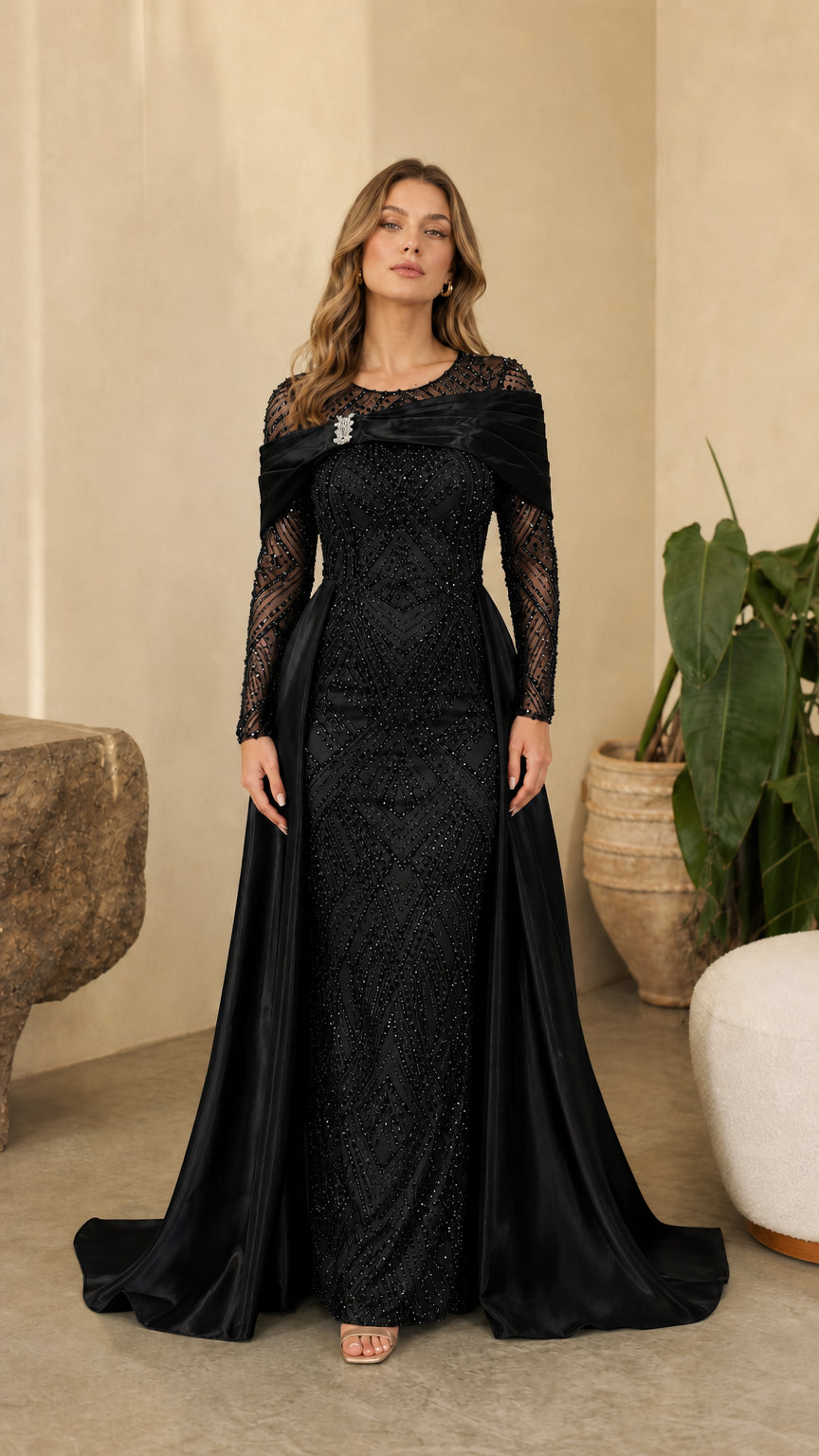 Full front view of model wearing Black sequined long sleeve evening gown with satin overskirt