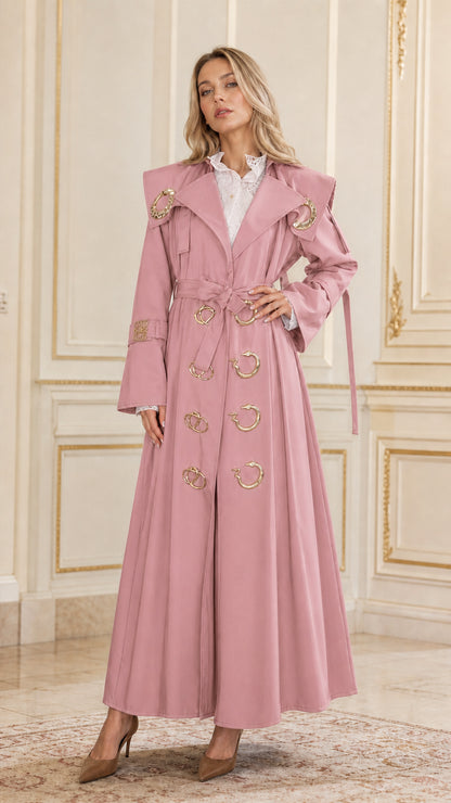 Front view of woman wearing dusty pink maxi belted trench coat with gold accents
