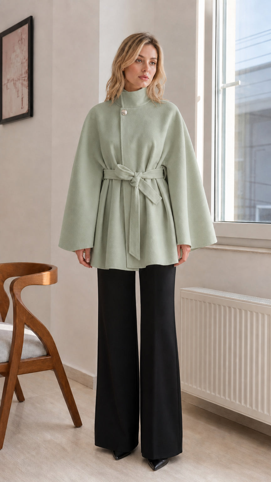 Sage green high-neck belted cape coat paired with tailored black pants