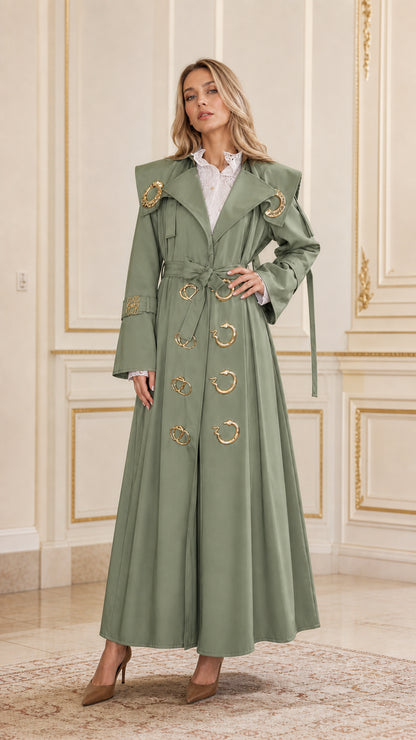 Front view of woman wearing sage green maxi belted trench coat with gold accents