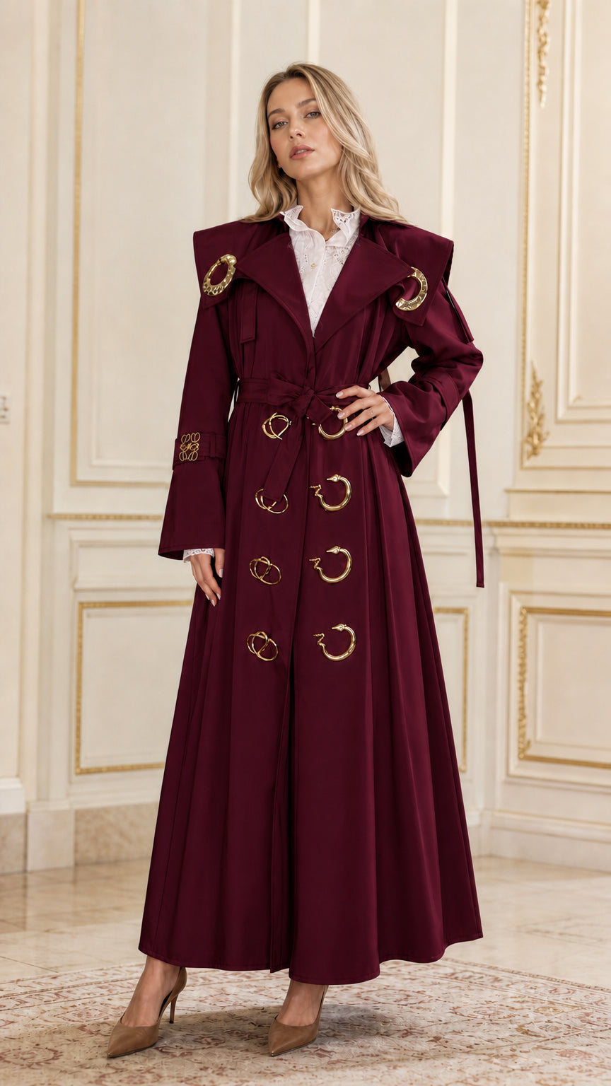 Front view of woman wearing burgundy maxi belted trench coat with gold accents