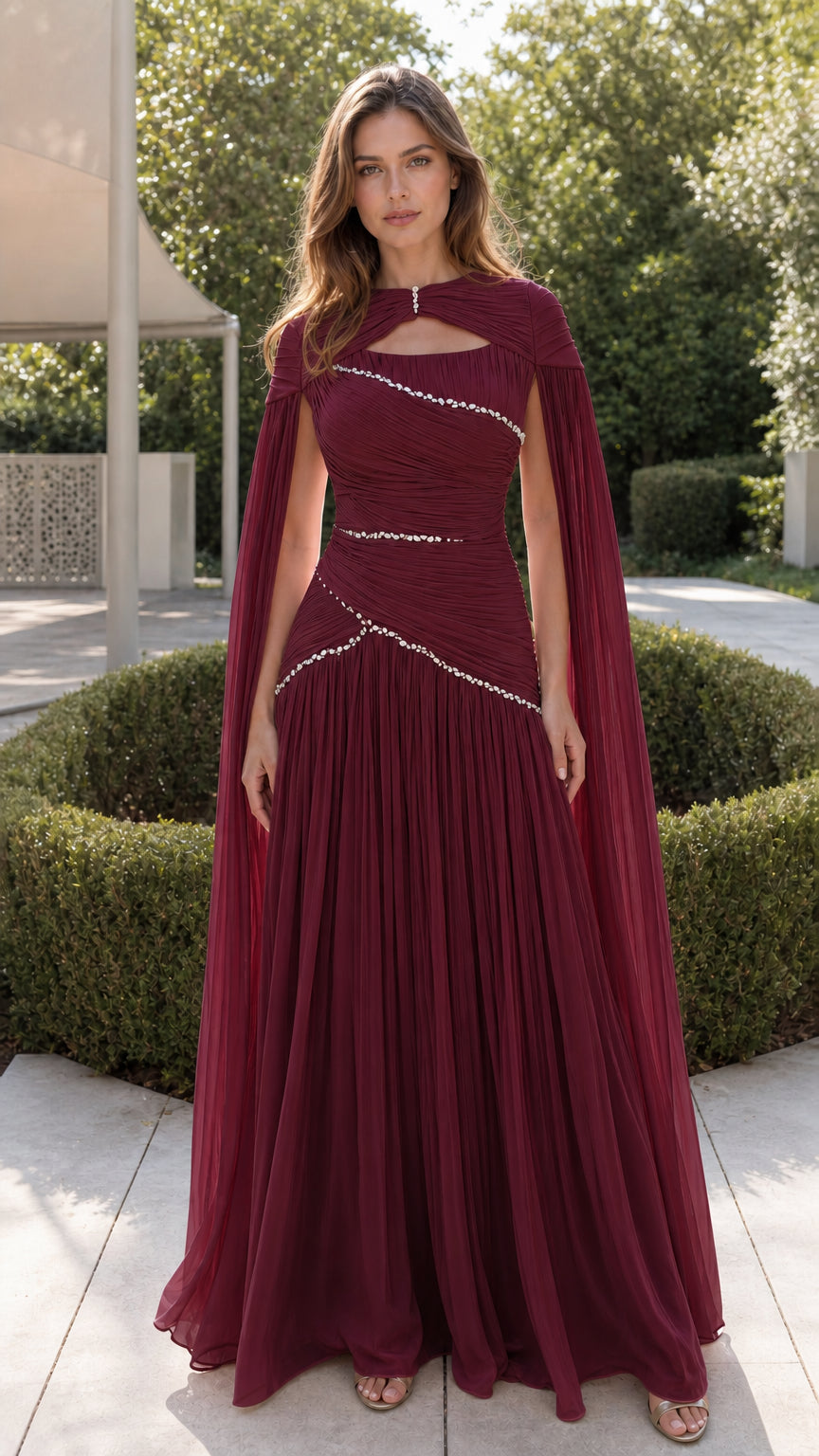Front view of rich burgundy pleated evening gown with cape and crystal embellishments